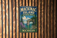 A vintage metal sign for Mackinac Island State Park in Michigan, featuring a scenic landscape with a rock arch and a body of water.