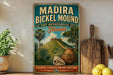 A vintage-style metal sign for Madira Bickel Mound, a state archaeological site in Florida, featuring a tropical landscape with palm trees, a castle, and a vase.