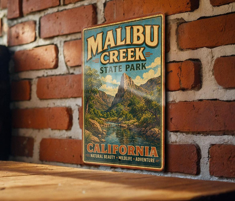 A vintage metal sign for Malibu Creek State Park, featuring a scenic landscape with mountains, water, and lush vegetation.