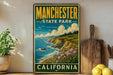 A vintage-style metal sign for Manchester State Park in California, featuring a scenic coastal landscape with cliffs, grass, and flowers.