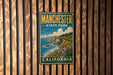 A vintage metal sign for Manchester State Park in California, featuring a scenic coastal landscape with cliffs, water, and flowers.