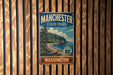 A vintage metal sign for Manchester State Park in Washington, featuring a scenic landscape with pine trees, a beach, and a mountain range.