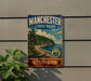 A vintage-style metal sign for Manchester State Park in Washington, featuring a scenic landscape with pine trees, a beach, and a mountain range.
