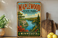 A vintage-style sign for Maplewood State Park in Minnesota, featuring a scenic landscape with a river, trees, and mountains.