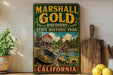 A vintage-style sign for Marshall Gold Discovery State Historic Park in California, featuring an illustration of a panning gold mine and a wooden bridge.