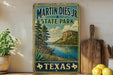 A vintage-style sign for Martin Dies Jr. State Park in Texas, featuring a scenic landscape with a lake, mountains, and trees.