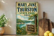 A vintage-style metal sign for Mary Jane Thurston State Park in Ohio, featuring a scenic landscape with a river, trees, and a sign that says "Nature is waiting".