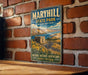 A vintage-style metal sign for Maryhill State Park in Washington, featuring a scenic landscape with a winding road, mountains, and a building.