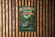 A vintage metal sign for Mashamoot Brook State Park, featuring a scenic illustration of a river and forest, mounted on a wooden wall.