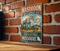 A vintage-style metal sign for the Mastodon State Historic Site in Missouri, featuring an illustration of a skeleton of a mastodon and a building.