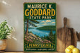 A vintage-style sign for Maurice K. Goddard State Park in Pennsylvania, featuring a scenic landscape with a lake and mountains.