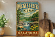 A vintage-style sign for McChee Creek State Park in Oklahoma, featuring a scenic landscape with a waterfall and flowers.