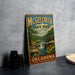 A vintage-style metal sign for McChee Creek State Park in Oklahoma, featuring a scenic landscape with a waterfall and flowers.