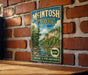 A vintage-style metal sign for Mcintosh Woods State Park in Iowa, featuring a scenic landscape with a river and trees.
