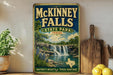 A vintage-style sign for McKinney Falls State Park in Texas, featuring a scenic illustration of a waterfall surrounded by lush greenery.