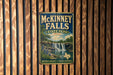 A vintage-style metal sign for McKinney Falls, a state park in Texas, is displayed on a wooden wall.