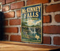 A vintage-style metal sign for McKinney Falls State Park in Texas, featuring a scenic image of the waterfall and surrounding landscape.