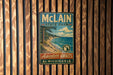 A vintage metal sign for McLain State Park, featuring a scenic landscape with a lake and mountains, hangs on a wooden wall.