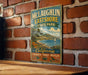 A vintage-style metal sign for McLaughlin Eastshore State Park, featuring a scenic landscape with a sailboat on the water and a mountain in the background.