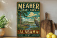 A vintage-style metal sign for Meacher State Park in Alabama, featuring a scenic illustration of a bird, a wooden dock, and a lake.