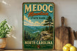 A vintage-style metal sign for Medoc Mountain State Park in North Carolina, featuring a scenic mountain landscape with pine trees and a river.