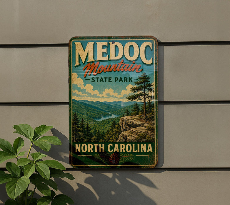 A vintage metal sign for Medoc Mountain State Park in North Carolina, featuring a scenic mountain landscape with pine trees and a river.