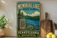 A vintage-style metal sign for Memorial Lake State Park in Pennsylvania, featuring a scenic landscape with a lake, mountains, and a stone wall.