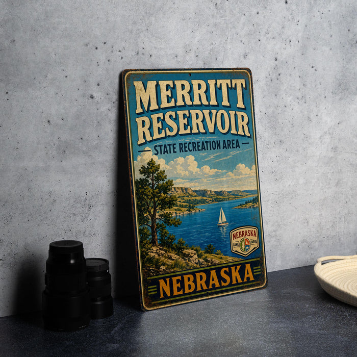 A vintage metal sign for the Merritt Reservoir, a state recreation area in Nebraska, featuring a scenic landscape with a lake, mountains, and a sailboat.