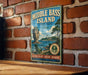 A vintage-style metal sign for Middle Bass Island, Ohio, featuring a scenic image of the island with a lighthouse and a rocky outcrop.