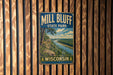 A vintage metal sign for Mill Bluff State Park in Wisconsin, featuring a scenic landscape with a river and mountains.
