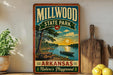 A vintage-style sign for Millwood State Park in Arkansas, featuring a scenic image of a lake, trees, and a picnic table.