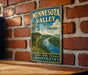 A vintage Minnesota Valley sign is displayed on a brick wall, featuring a scenic landscape with a river and lush greenery.