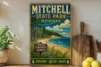 A vintage-style metal sign for Mitchell State Park in Michigan, featuring a scenic landscape with a beach, pine trees, and a lake.