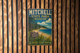 A vintage metal sign for Mitchell State Park in Michigan, featuring a scenic landscape with pine trees, a beach, and a lake.