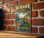 A vintage-style metal sign for Mohawk Park, Oklahoma, featuring a scenic landscape with a lake and mountains.
