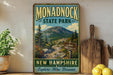 A vintage-style sign for Monadnock State Park, featuring a mountain landscape and trail signs, is displayed on a shelf next to a wooden cutting board and some lemons.