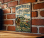 A vintage metal sign for Monmouth Battlefield State Park in New Jersey, featuring a historical illustration of a battle scene with soldiers and a cannon.
