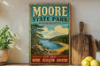 A vintage metal sign for Moore State Park in Massachusetts, featuring a scenic landscape with a lake and mountains.