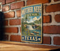 A vintage-style metal sign for Mother Neff State Park in Texas, featuring a scenic landscape with a waterfall and greenery.
