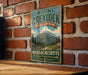 A vintage metal sign for Mount Greylock State Reserve in Massachusetts, featuring a mountain landscape and the text "The Highest Peak in Massachusetts".