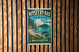 A vintage-style sign for Mystery Bay State Park in Washington, featuring a scenic landscape with a beach, mountains, and a body of water.