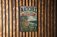 A vintage metal sign for Natchez State Park, Mississippi, featuring a scenic landscape with a river and trees.