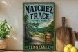 A vintage-style sign for Natchez Trace State Park in Tennessee, featuring a scenic road surrounded by trees and mountains.