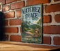 A vintage-style metal sign for Natchez Trace State Park in Tennessee, featuring a scenic landscape with a winding road and lush greenery.