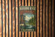 A vintage-style metal sign for Navarro River Redwoods State Park in California, featuring a scenic image of the river surrounded by redwood trees.