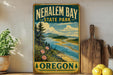 A vintage-style metal sign for Nehalem Bay State Park in Oregon, featuring a scenic landscape with mountains, a river, and a beach.