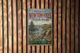A vintage-style metal sign that reads "Welcome to Newton Hills State Park" is displayed on a wooden wall.