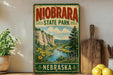 A vintage-style sign for Niobrara State Park in Nebraska, featuring a scenic landscape with a river, mountains, and wildflowers.