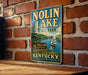 A vintage-style sign for Nolin Lake State Park in Kentucky, featuring a scenic image of a lake with a sailboat and surrounded by trees.