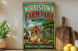A vintage-style metal sign for Norristown Farm Park, featuring illustrations of farm animals and a barn, is displayed on a shelf next to a wooden cutting board and some lemons.